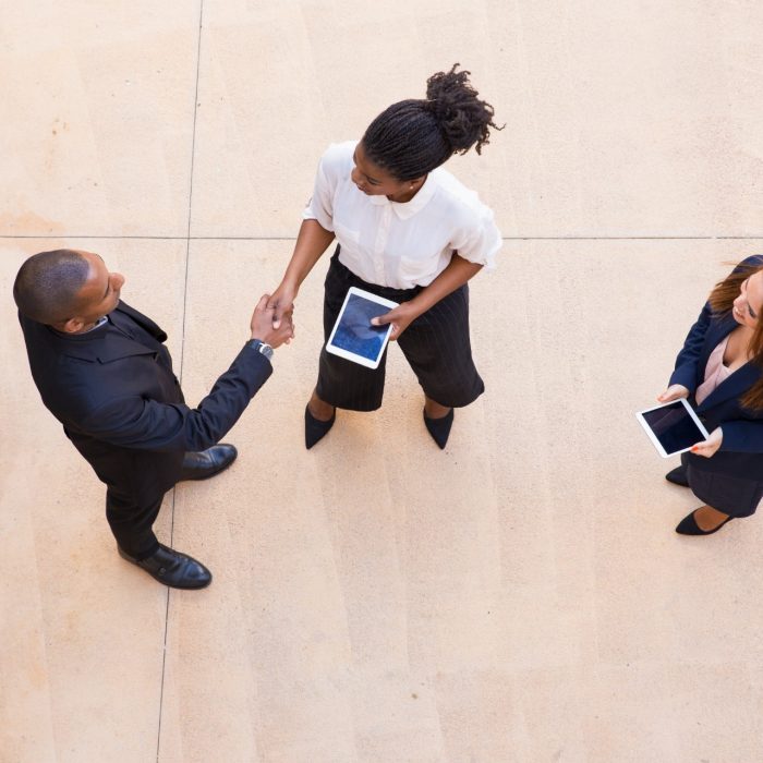 Learn to lead 3 business people with iPads talking and shaking hands dressed in business attire
