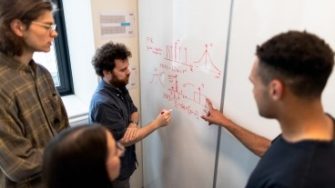 Engineering students writing on whiteboard four Engineering students writing on and viewing whiteboard