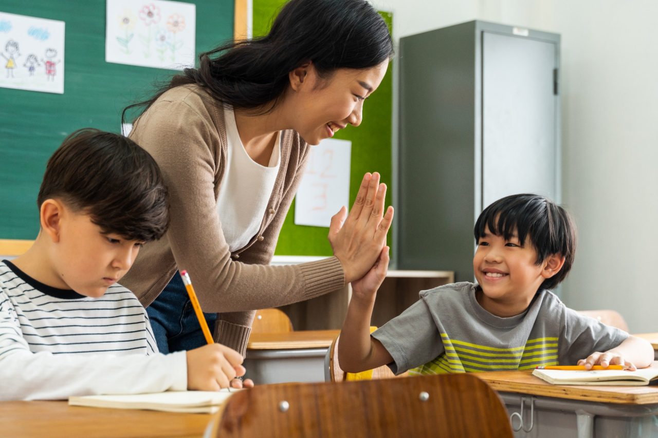 Young Asian teacher giving boy high five in school, success, achievement, happiness. Asia school boy with young woman in class.